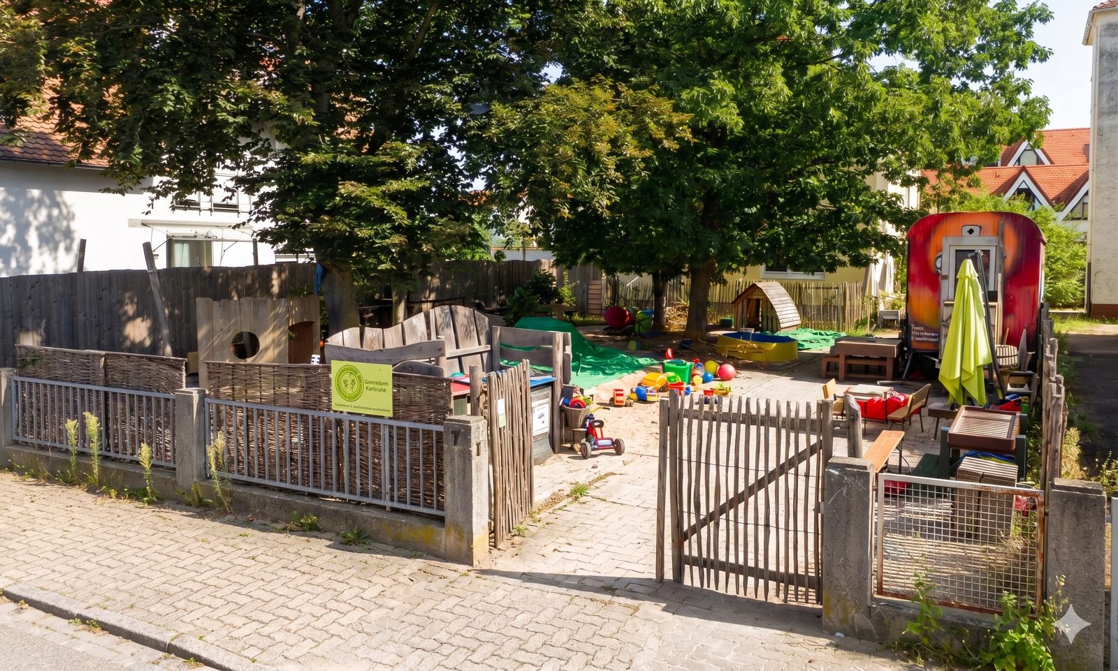 Unser naturnahes Aussengelaende in Karlsruhe-Neureut mit Holzzaun, Sandkasten und viel Platz zum Spielen unter alten Baeumen
